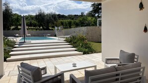 Ein überdachter Außenbereich mit Pool, Treppen zum Pool und Gartenmöbeln.