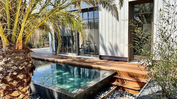 A modern house with a glass facade, a swimming pool, and a wooden deck.