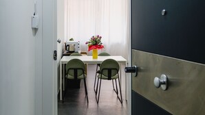 Un couloir étroit mène à un coin repas où se trouvent une table et des chaises, une machine à café et un vase rempli de fleurs.