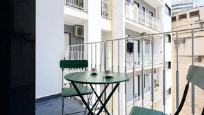 Un balcon doté d’une table et de chaises en verre, offrant une vue sur un immeuble comportant de nombreux balcons et garde-corps.