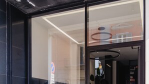 Entrada de un edificio moderno con puertas de vidrio, un letrero de estacionamiento visible y una escalera que conduce al interior.