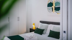 Una cama bien hecha con almohadas, una lámpara de noche y una manta verde.