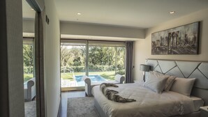 A modern bedroom with a large bed, a painting, and a view of a swimming pool.