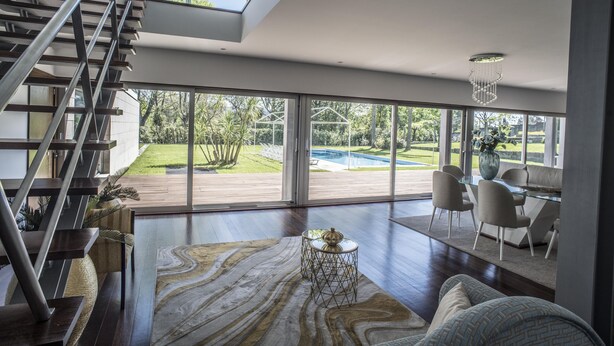 A spacious living area with a modern staircase, large windows, and a view of a backyard.