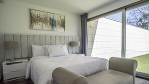 A modern bedroom with a large bed, two bedside tables, a sofa, and a large window offering a view of the outdoors.