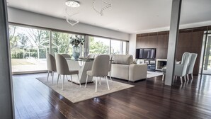 A modern living room with a dining area, large windows, and a flat-screen TV.