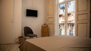 A bedroom with a bed, a chair, a television, and a view of an outdoor balcony. - B&B U'Panare, in Taranto's historic center a structure reminiscent of home (Taranto)
