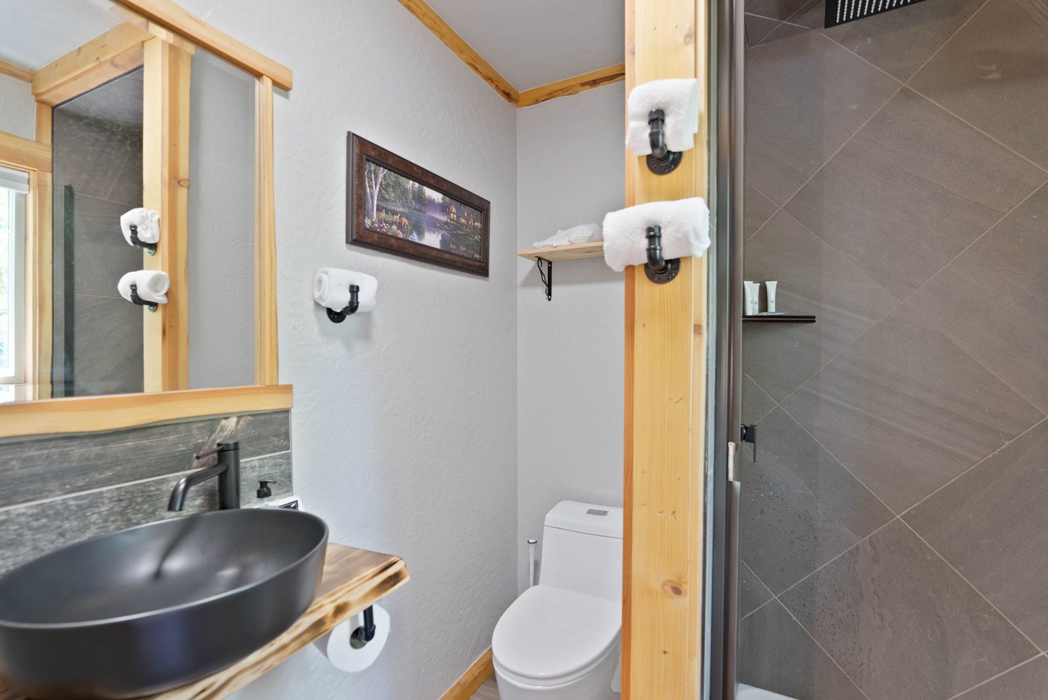 A bathroom with a wooden vanity, a large mirror, a toilet, and a shower area.