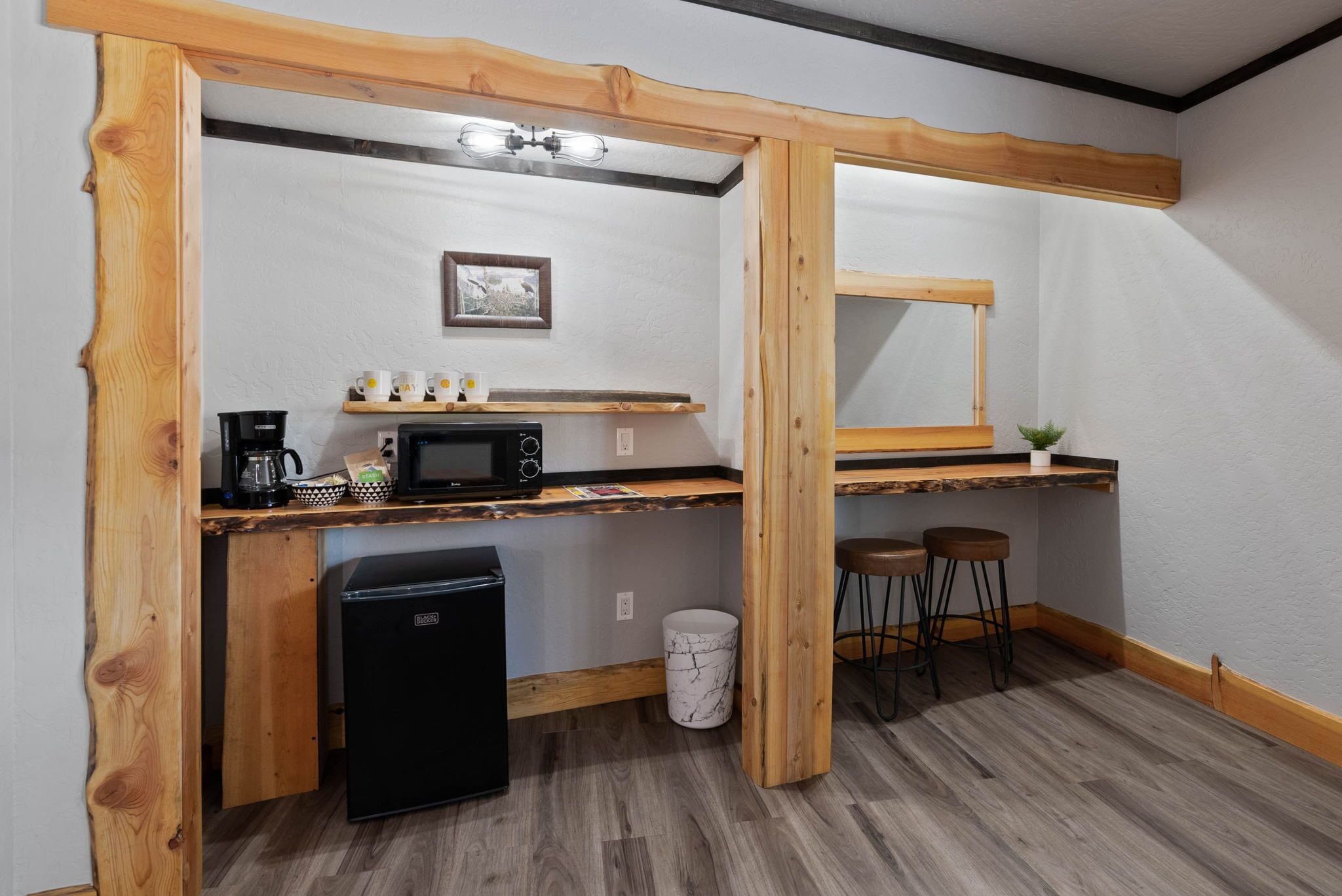 A compact kitchen with a built-in microwave, coffee maker, and a small refrigerator. There are wooden shelves above the counter and a single chair.