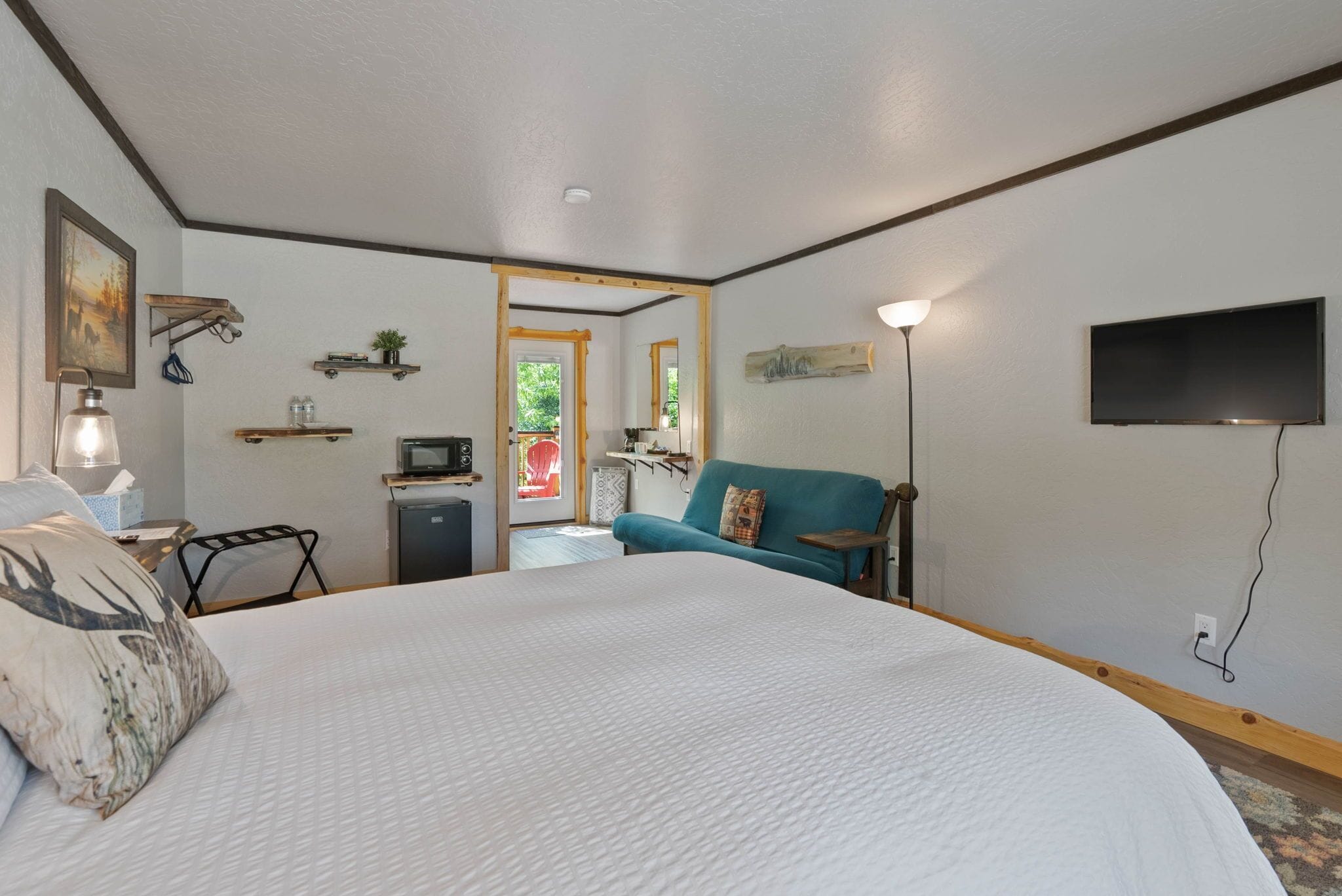 Una camera d'albergo con un letto grande, una televisione, una scrivania con una lampada, un angolo cottura e vista all'esterno.