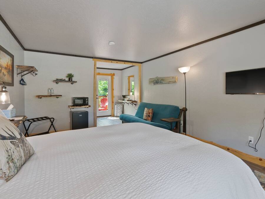 Una camera d'albergo con un letto grande, una televisione, una scrivania con una lampada, un angolo cottura e vista all'esterno.
