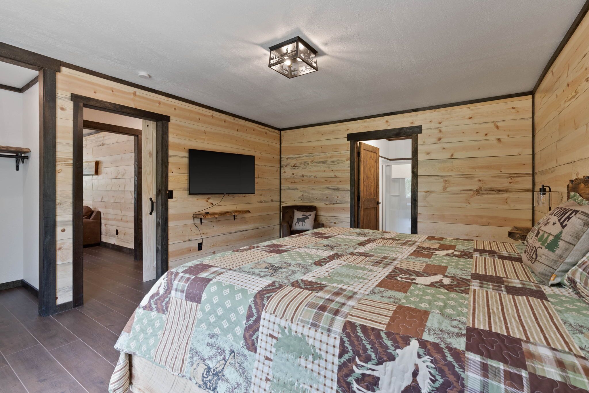 Une pièce aux murs en bois, avec un grand lit recouvert d’une courtepointe à motifs, un téléviseur à écran plat et un luminaire fixé au plafond.