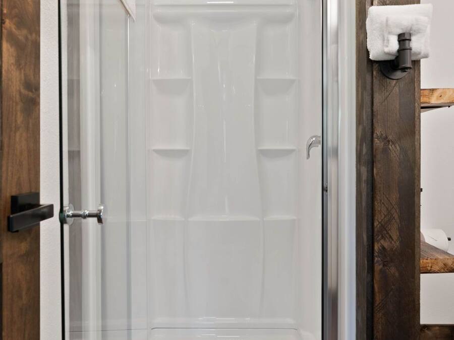Divisória de chuveiro com paredes de vidro, interior branco, moldura de porta de madeira e porta-toalhas na parede.