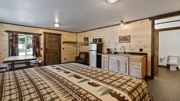 A cozy room with a bed, a dining table, a kitchen area with a refrigerator and microwave, and a bathroom with a toilet.
