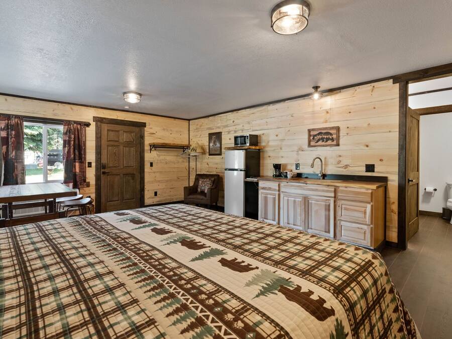 A cozy room with a bed, a dining table, a kitchen area with a refrigerator and microwave, and a bathroom with a toilet.