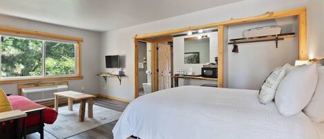 Une chambre avec un grand lit, un bureau en bois, une chaise, une petite table, un téléviseur et une fenêtre donnant sur un paysage verdoyant.