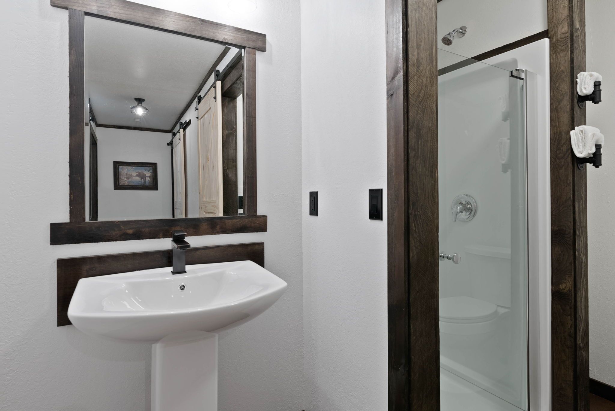Un baño con lavamanos blanco, espejo y cabina de ducha con mampara de vidrio.