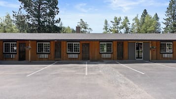 A motel with a row of rooms, each with a window and a door. There is a parking lot in front of the building.