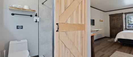A bathroom with a shower, toilet, and a wooden door.