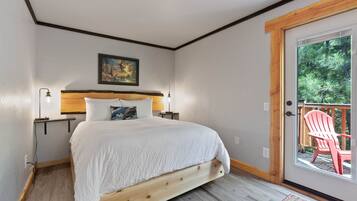 Un dormitorio con una cama de madera, un cuadro en la pared, una mesita de noche y una puerta que da a un espacio exterior con una silla.
