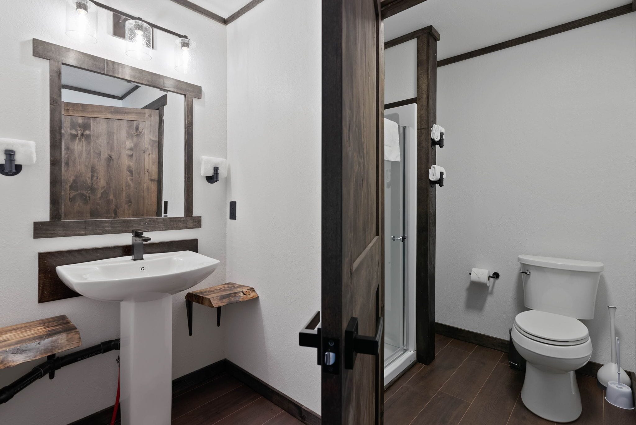 A modern bathroom with a wooden vanity, a white sink, a toilet, and a glass shower enclosure.