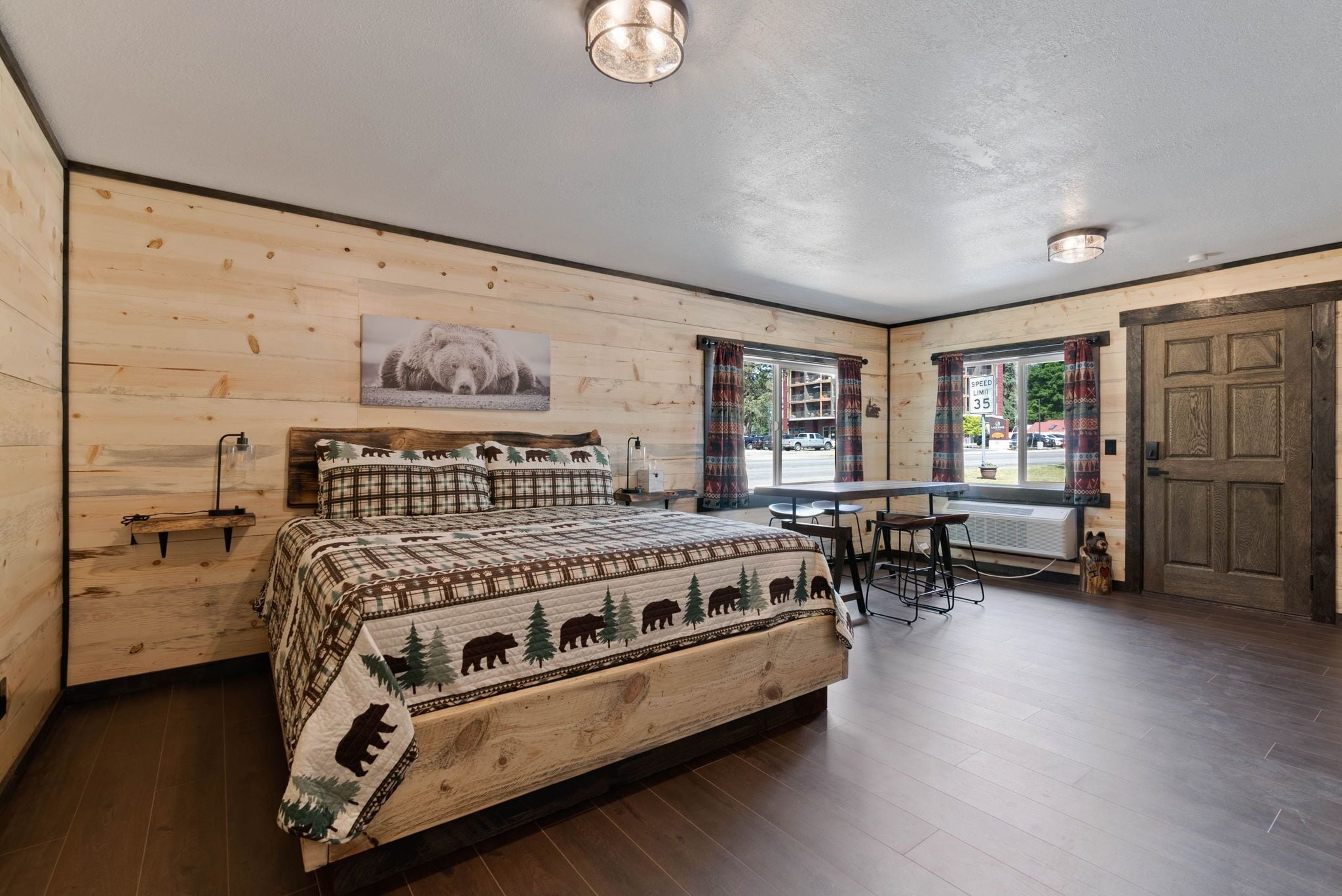 Una habitación con paneles de madera, una cama, una mesa y un ventanal con cortinas.