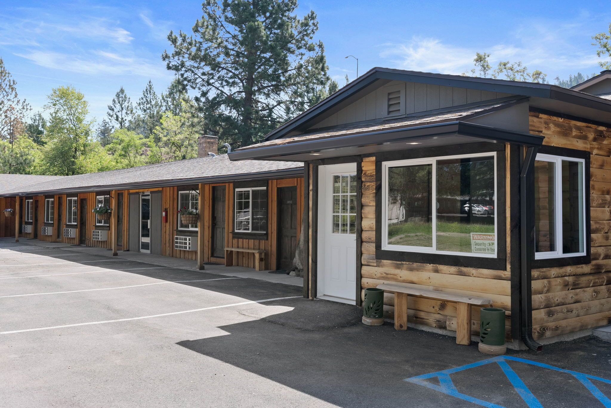 A row of log cabin-style rooms with large windows, a covered outdoor seating area, and a parking lot.
