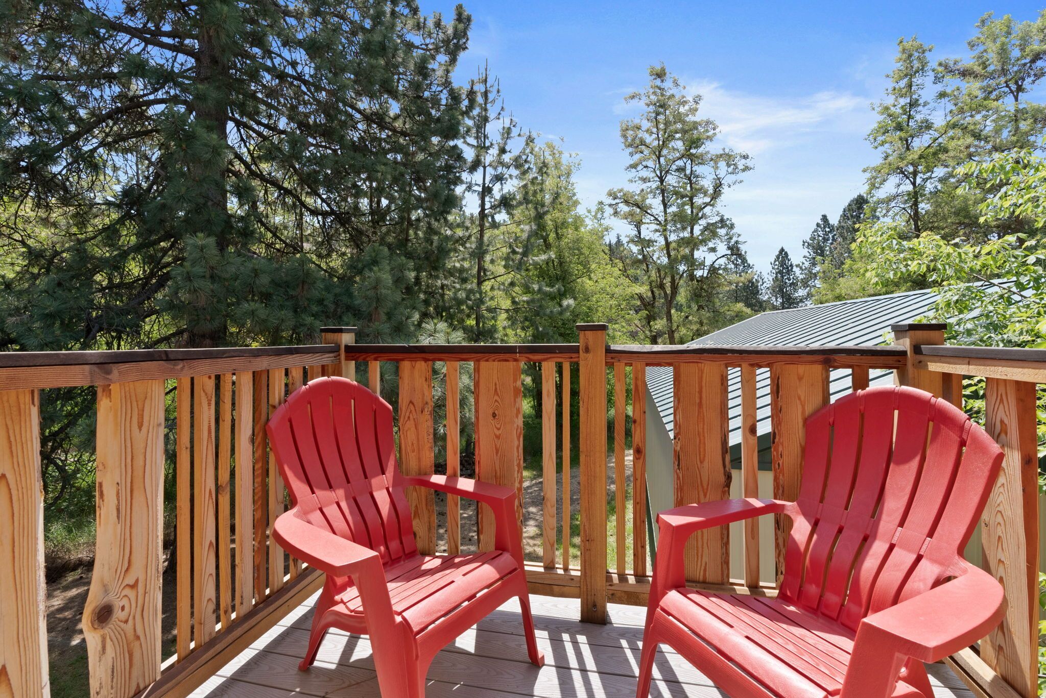 A wooden deck with two red Adirondack chairs and a wooden railing.