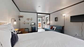 Habitación de hotel con una cama grande, un escritorio con computadora, un sofá y un televisor montado en la pared.