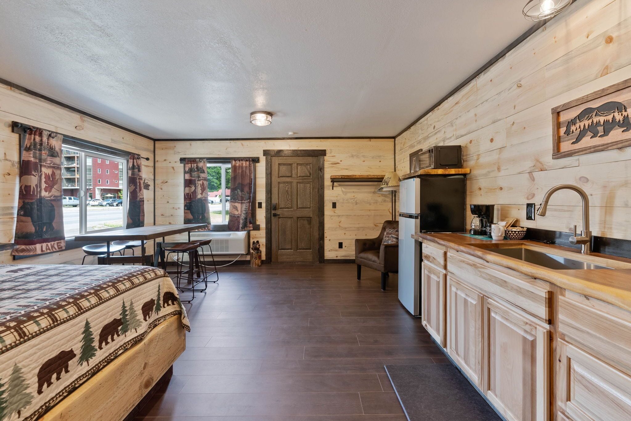 A room with a bed, a dining table, a kitchen area, and a door leading to another room.