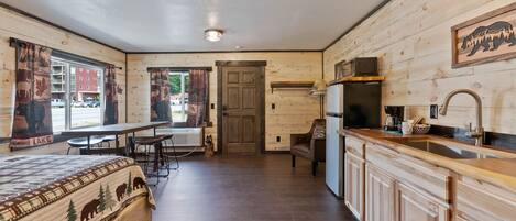 A room with a bed, a dining table, a kitchen area, and a door leading to another room.