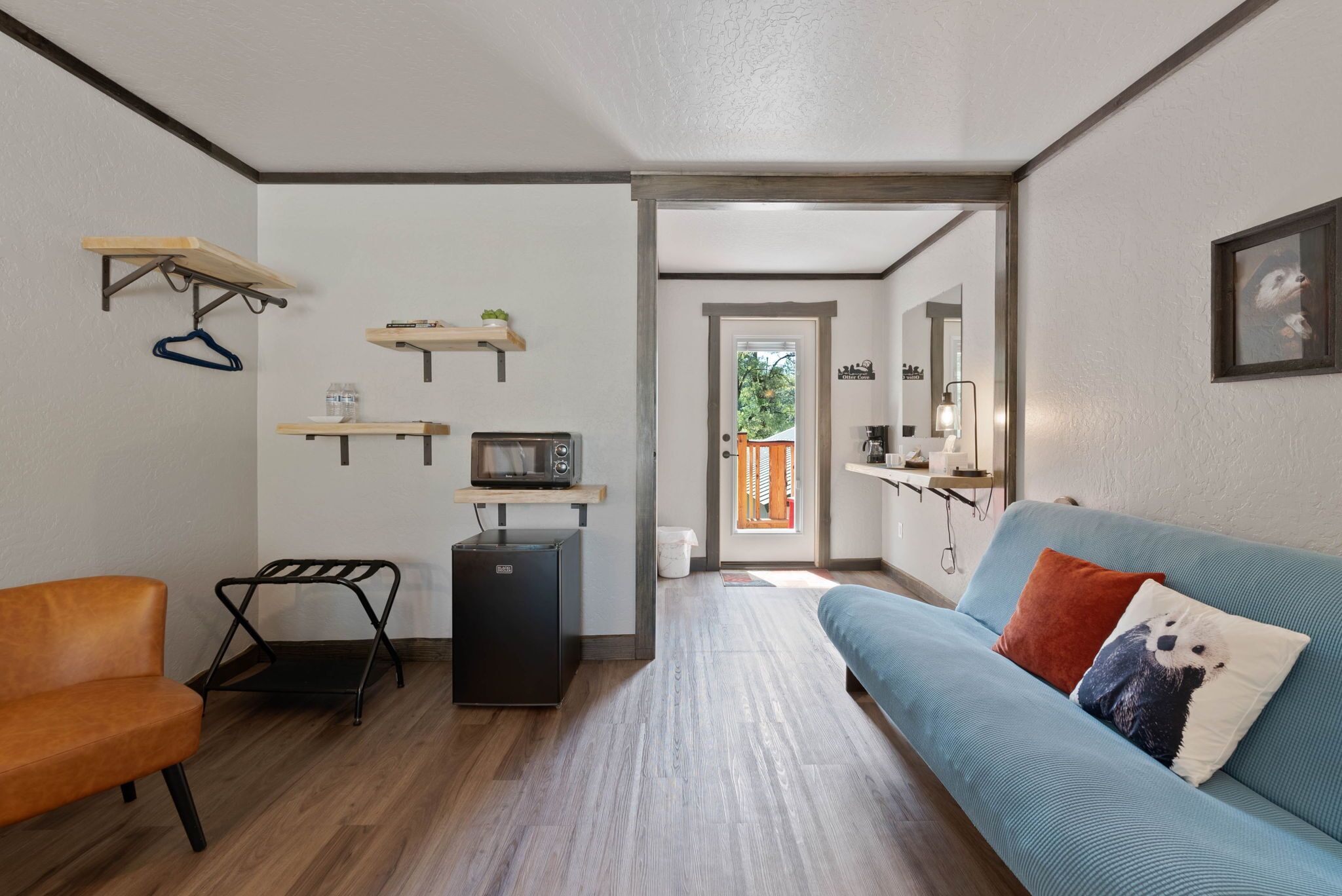 A compact living space with a sofa, a chair, a small kitchenette, and a door leading to an outdoor area.