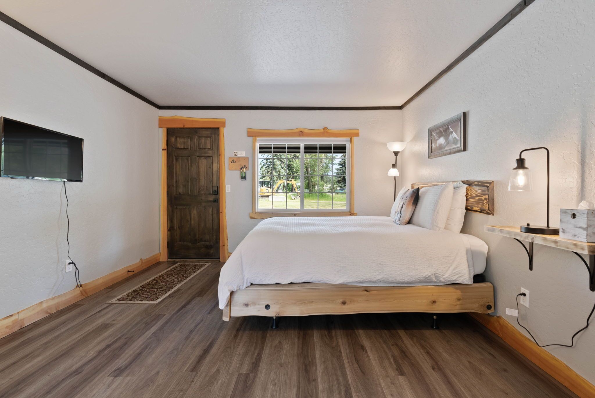 Un dormitorio con cama de madera, ventana con vistas, puerta y televisor montado.