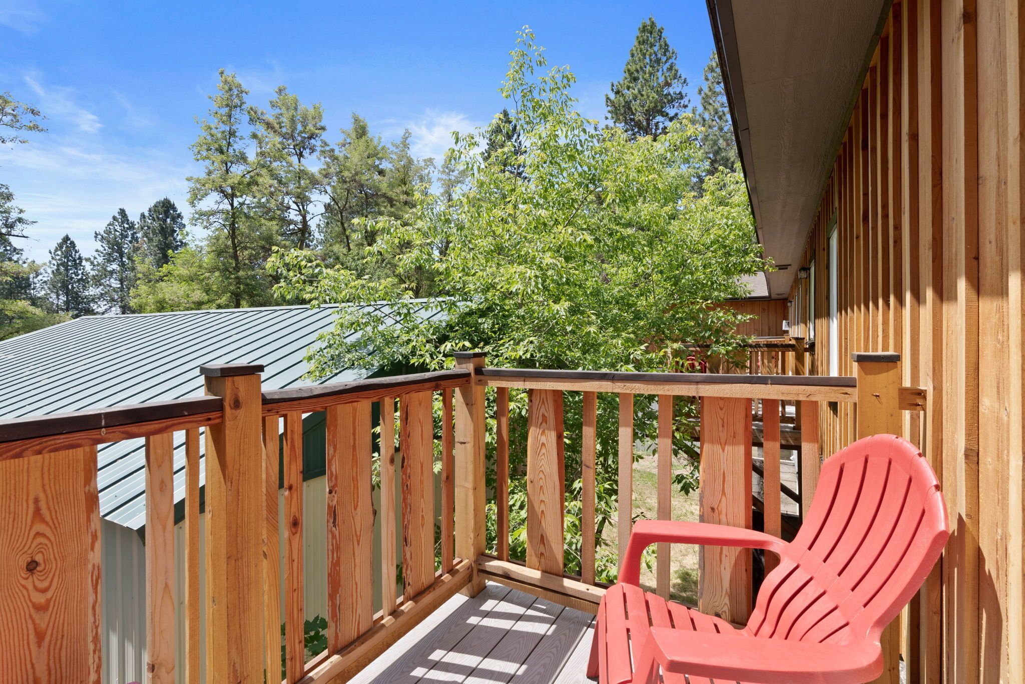 A wooden deck with a red chair, surrounded by trees and a building with a sloped roof.