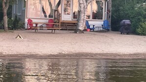 En hytte ved søen med en overdækket terrasse, udendørs møbler og bålsted.