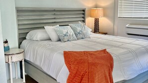 A bedroom with a bed, a ceiling fan, a bedside table with a lamp, and a window with blinds. - Tropical Hideaway in Downtown Flagler Beach (Flagler Beach)