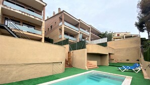 Ein Schwimmbecken mit einer grünen Rasenfläche, einer Treppe zu einem Balkon und einem Gebäude mit mehreren Balkonen und einer Ziegelaußenwand.