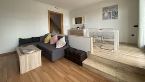 Ein modernes Wohnzimmer mit grauem Sofa, Holztisch und einem klaren Esstisch mit Stühlen.