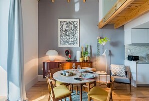 A dining area with a round table set for four, surrounded by chairs. A large abstract artwork hangs on the wall above the table.