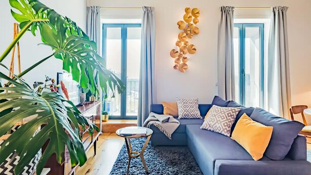 Un soggiorno moderno con un divano blu, una pianta verde di grandi dimensioni e un elemento decorativo a parete.
