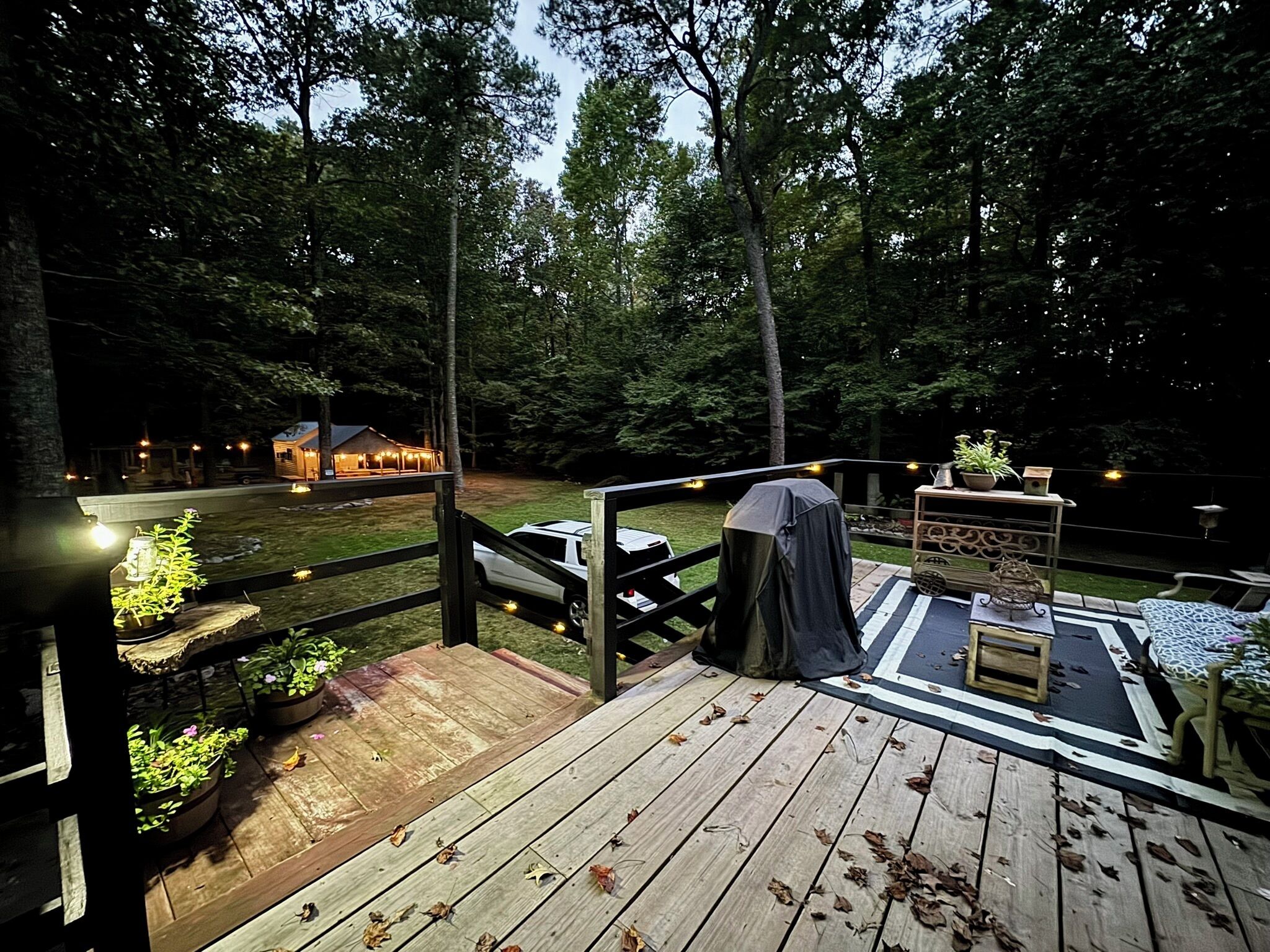 A wooden deck with a barbecue area, potted plants, and a view of a house in the background.