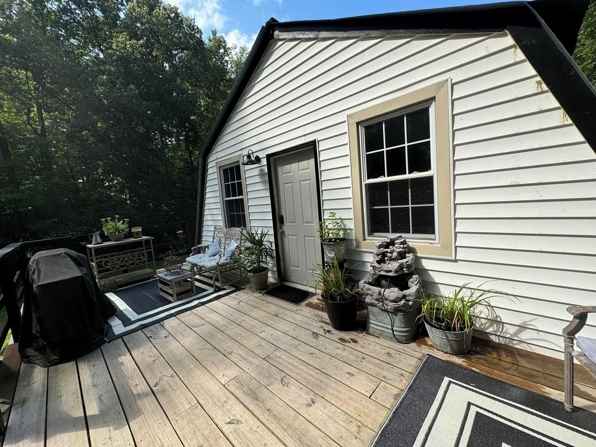 A wooden deck with outdoor furniture, a covered grill, and potted plants.