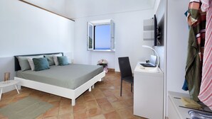 A bedroom with a bed, a desk with a laptop, a chair, a TV, and a window with a view.