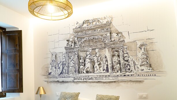 A bedroom with a mural of an ancient gate, a bed with pillows, a bedside lamp, and a wooden door. - ALFICEN CERVANTES 5 COLLECTION (Toledo)