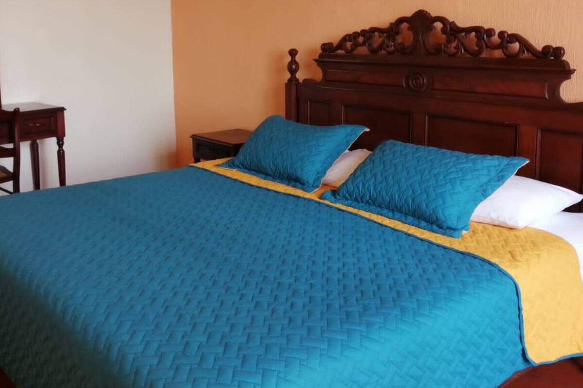 A bed with a blue quilt and a yellow accent, a wooden headboard, and a nightstand with a lamp.