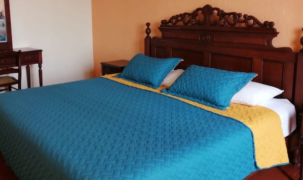 A bed with a blue quilt and a yellow accent, a wooden headboard, and a nightstand with a lamp.