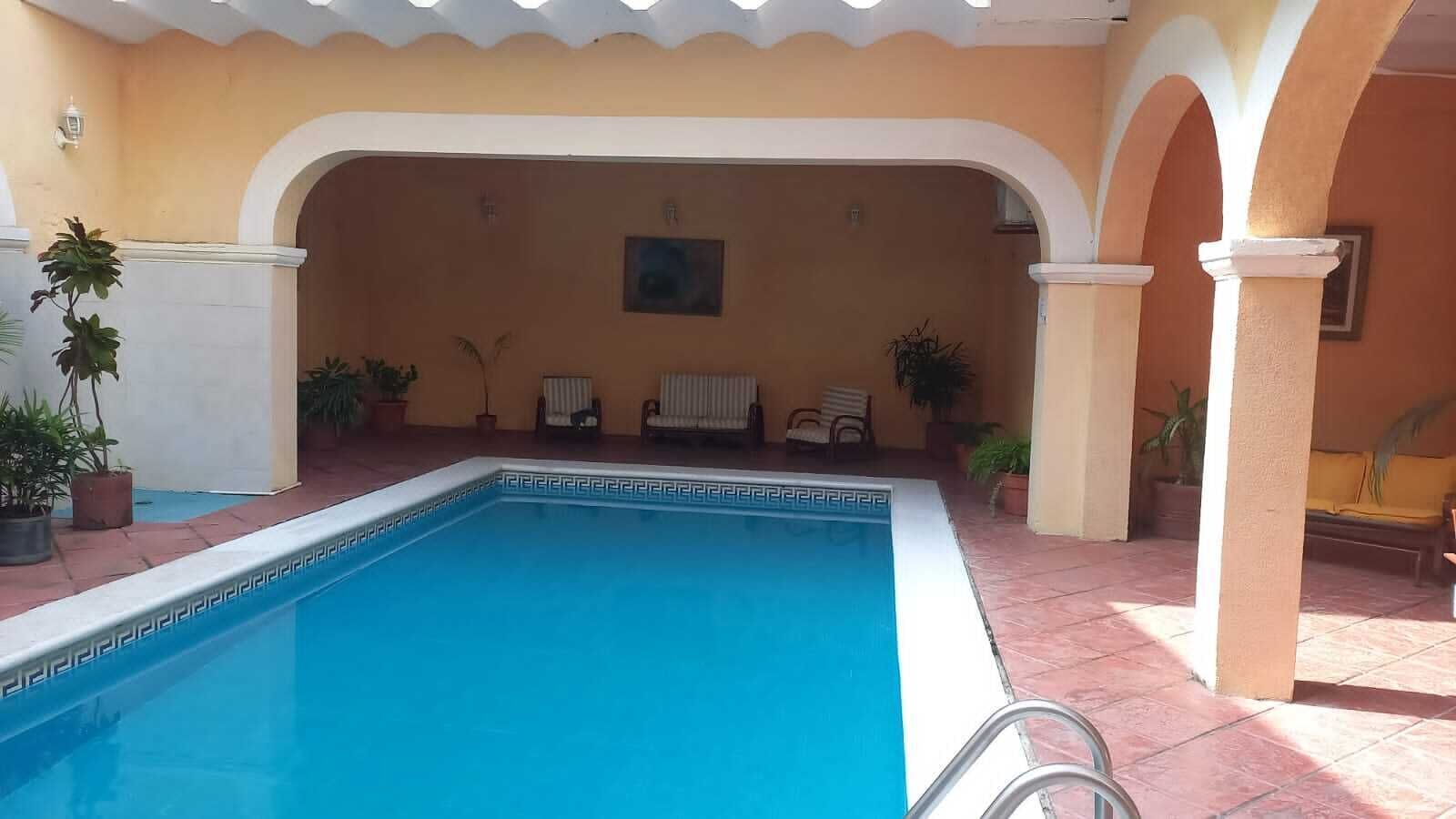 En swimmingpool med flisepyntet solterrasse, omgivet af plantekrukker og et par stole.