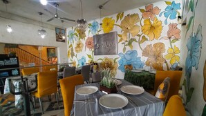 A restaurant with a floral wall mural, yellow chairs, and a table set for two. - Hotel Posada Doña Lala (Tlacotalpan)