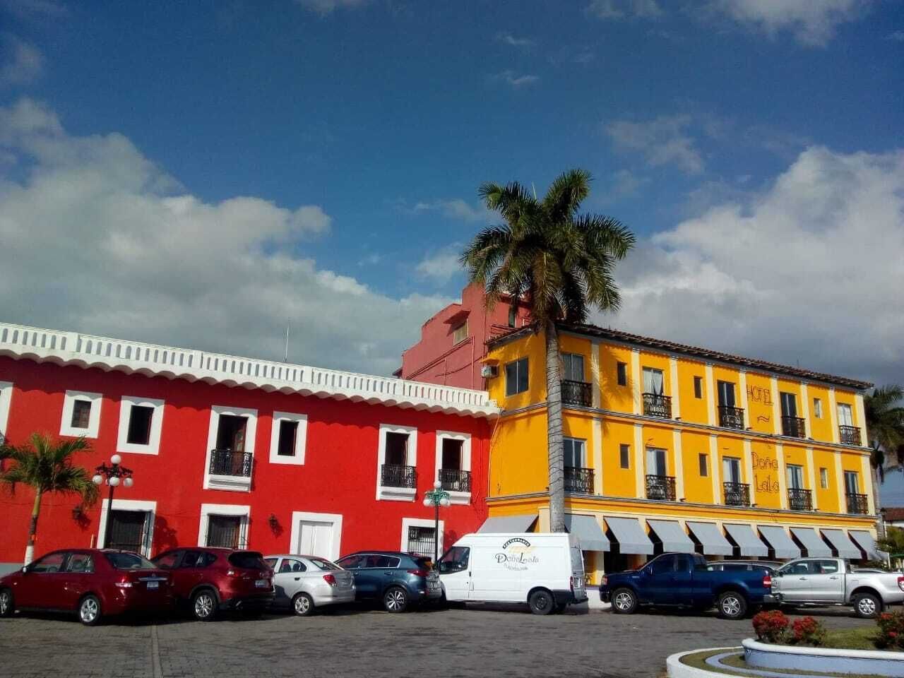 Ein zweistöckiges Hotel mit roter und gelber Fassade, mehreren Balkonen und parkenden Autos davor.