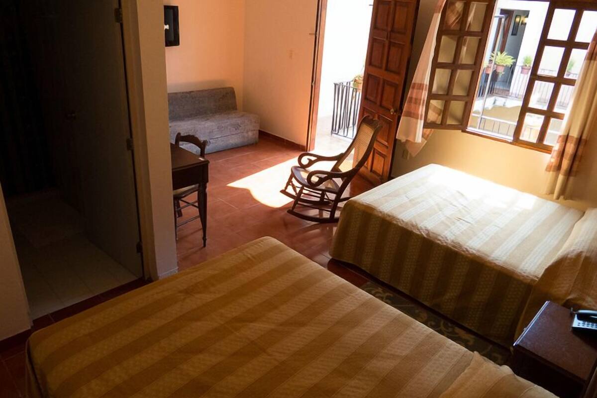 A room with two beds, a wooden rocking chair, a small table, and a balcony with a railing.